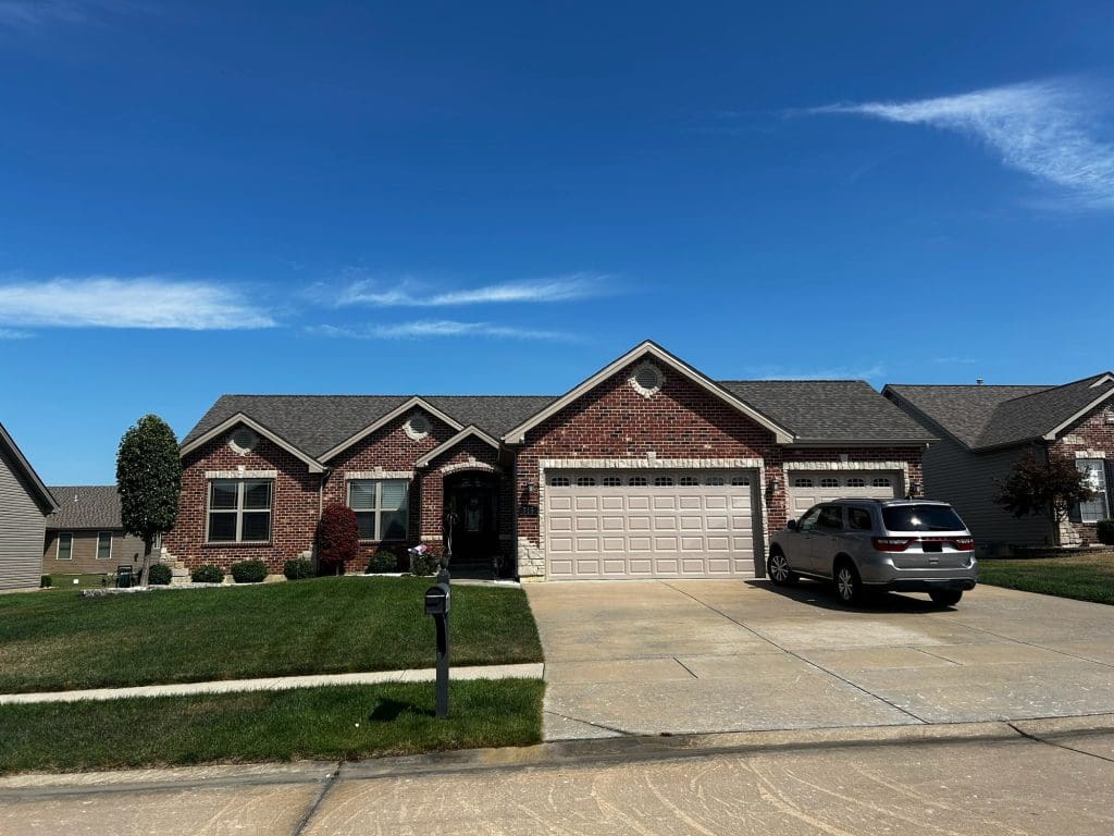 St. Louis single-story brick home with two-car garage, perfect for roofing, siding, or gutter upgrades. Sunny, well-kept lawn.