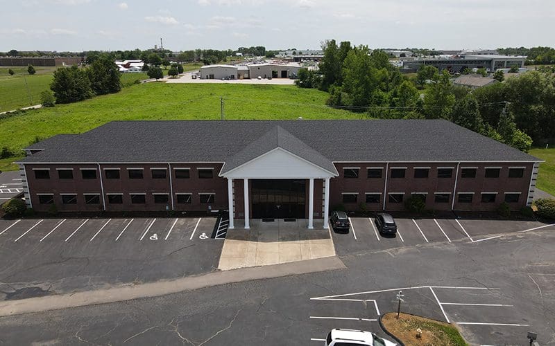 Aerial view of a brick office building in Greater St. Louis with new roofing, siding, and gutters; parking and greenery visible.